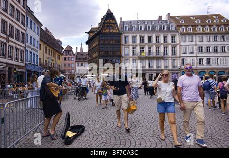 STRASBOURG, FRANKREICH - 6. AUGUST 2026 - Menschen gehen auf einem Kopfsteinpflasterplatz in Straßburg, während ein Straßenmusiker auftritt Stockfoto