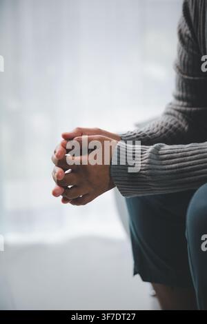 Nahaufnahme seitlich von einem Erwachsenen, der mit verschränkten Händen sitzt und Angst, Stress, Unsicherheit oder stilles Nachdenken ausdrückt, mit großzügigem Kopierraum f Stockfoto