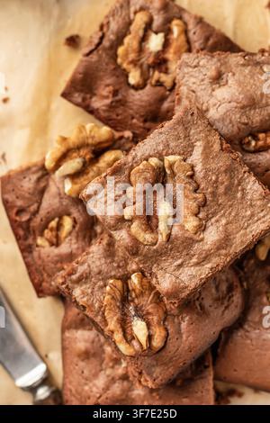 Schokoladen-Walnuss-Brownie-Stücke in einem Stapel auf Pergamenthintergrund, Nahaufnahme, Oberblick. Konzept für Heimbäckerei, Rezept Stockfoto