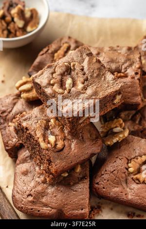 Schokoladen-Walnuß-Brownie-Stücke in einem Stapel auf Pergamenthintergrund, Nahaufnahme. Konzept für Heimbäckerei, Rezept Stockfoto