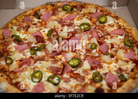 Frische köstliche Pizza mit Peperoni, Schinken, Ananas und Jalapeño auf Karton. Stockfoto