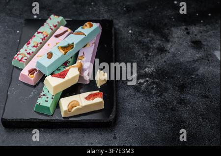 Verschiedene bunte handwerkliche Schokoladentafeln mit getrockneten Früchten und Nüssen auf dunklem Steinhintergrund, handwerklich hergestellte Gourmet-Süßwaren. Stockfoto