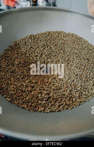 Ungeröstete grüne Kaffeebohnen fallen in den Trichter einer kommerziellen Kaffeeröstmaschine, die Bewegung während der Beladungsphase des Röstvorgangs wird festgehalten Stockfoto