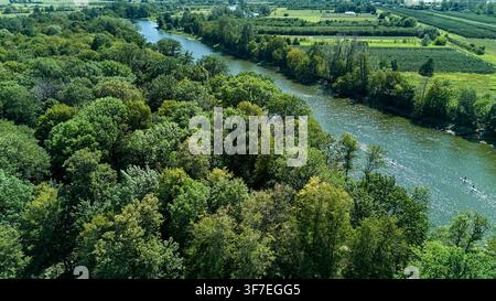 Luftbild zeigt einen Fluss, der sich durch üppige Grünflächen windet. Bäume säumen beide Ufer, lebendig und voller Leben. Fischerboote zieren die Wasseroberfläche, motio Stockfoto