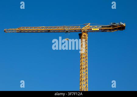 Gelber Turmdrehkran im Profil mit Ausleger, Gegenausleger und Haken vor klarem Himmel Stockfoto