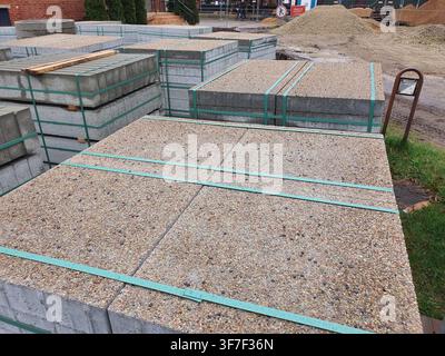 Mehrere Stapel von Betonpflasterplatten mit freigelegtem Aggregatfinish sind im Freien auf einer Baustelle oder in einem Baumateriallager gelagert. Die Stockfoto