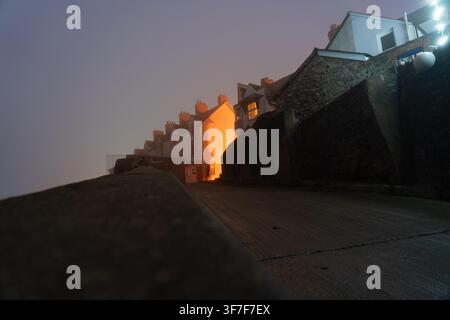 Der Abendnebel schafft einen stimmungsvollen Kontrast zur warmen Beleuchtung des Hauses in der West Street, Watchet, Somerset, und fängt den stillen Charme der Stadt ein. Stockfoto