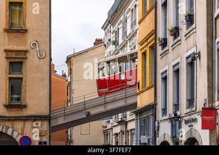 Lyon, Frankreich – 27. Juli 2026: Rote Standseilbahn überquert eine erhöhte Eisenbahnbrücke über eine schmale Straße im historischen Vieux Lyon. Stockfoto