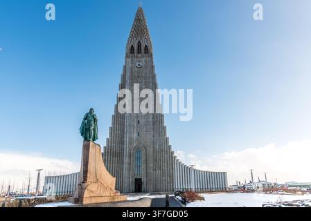 Die Bronzestatue von Leif Erikson steht auf dem verschneiten Platz vor der imposanten Betonfassade der Hallgrímskirkja in Reykjavík, mit Stockfoto