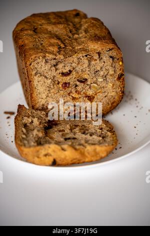 Nahaufnahme eines hausgemachten Vollkornbrotlaibs und einer Scheibe auf einem weißen Teller Stockfoto