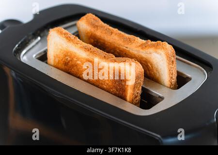 Goldene Brotscheiben steigen auf, rösten und bräunen sich in einem schwarzen elektrischen Toaster in einer hellen Küche, Frühstücksessen, Hausmannskost. Stockfoto