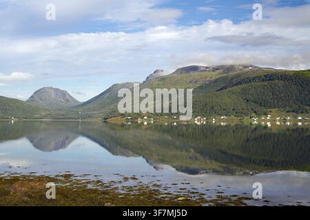 Ein ruhiger See mit Reflexionen der Berge und des Himmels. Kleine Siedlung im Hintergrund, Botnhamm, Troms, Senja, Norwegen Stockfoto