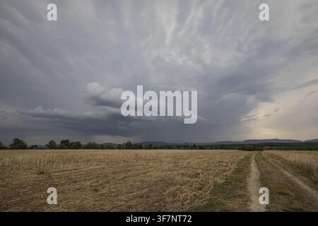 Dramatische dunkle Gewitterwolken sammeln sich über einem abgeernteten Stoppelfeld mit einem Feldweg, der zur Schwäbischen Alb in Deutschland führt Stockfoto
