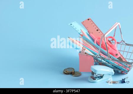 Zurück-zur-Schule-Einkäufe mit Schreibwaren in einem Miniatur-Einkaufswagen auf blauem Hintergrund Stockfoto