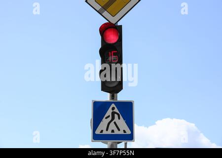 Rote Ampel mit Countdown-Timer und Fußgängerüberquerungszeichen vor einem klaren blauen Himmel, Rote Ampel mit einem digitalen Countdown-Timer, der anzeigt Stockfoto