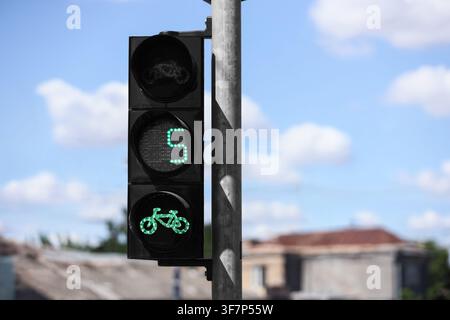 Grüne Fahrradampel mit Countdown-Timer, der die Zahl fünf anzeigt, vor einem blauen Himmel mit Wolken; dieses urbane Infrastruktur-element fördert den Straßenverkehr Stockfoto