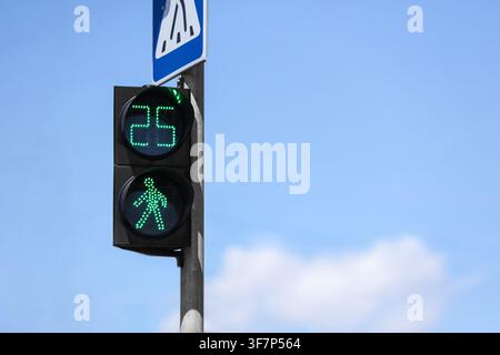 Grüne Fußgängerampel mit Countdown-Timer, der 25 Sekunden anzeigt, und Zebrastreifenzeichen vor einem blauen Himmel, das Signal ist an einem Mast montiert gegen den Stockfoto