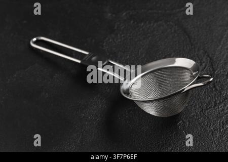 Edelstahl-Teesieb mit feinem Netz und Griff auf einem dunklen strukturierten Hintergrund, Küchenutensil zum Sieben von Zutaten Stockfoto