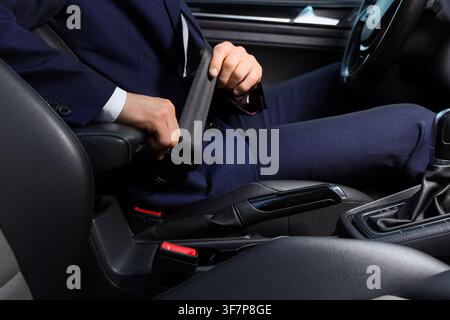 Geschäftsmann in einem dunklen Anzug, der seinen Sicherheitsgurt in einem modernen Auto schließt, betont Sicherheit und verantwortungsvolles Fahren, diese Handlung unterstreicht die Wichtigkeit Stockfoto