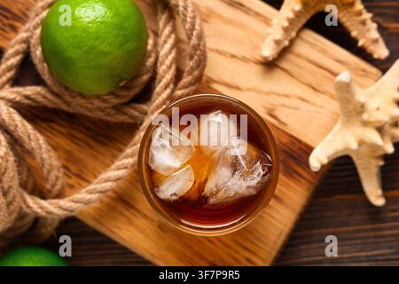 Bord mit einem Glas kalten Cuba Libre Cocktail, Sternenfischen und Seil auf hölzernem Hintergrund Stockfoto