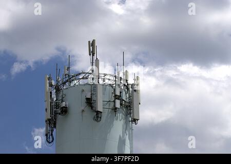 Ein Telekommunikationsantennenarray, das auf der Spitze eines Wasserturms montiert ist, vor einem bewölkten Himmel. Stockfoto