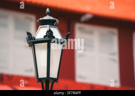Eine vertikal ausgerichtete Mittel-Nahaufnahme eines klassischen schwarzen ornamentalen Straßenlaternen mit mattierten Glasscheiben. Die Laterne hebt sich von einem weichen Stockfoto