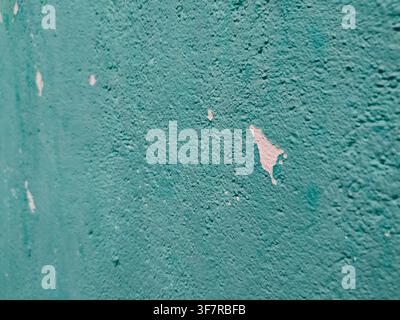 Eine Nahaufnahme einer texturierten türkis gestrichenen Wand mit kleinen Stellen abblätternder Farbe, die das darunterliegende Weiß freilegen. Stockfoto