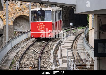 Lyon, Frankreich - 27. Juli 2026: Roter Standseilbahnzug steigt steile Außenschienen nahe steinernen Torbögen auf der Fourviere-Hochbahnlinie hinauf. Stockfoto