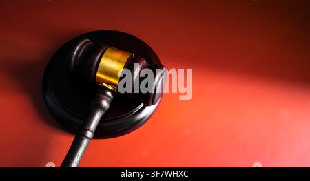 Nahaufnahme eines hölzernen Richterhammer mit goldenem Band auf leuchtend rotem Hintergrund, Konzept für Gerichtsjustiz und rechtliche Autorität Stockfoto