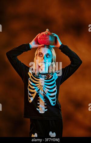 Kind in Skelettkostüm, das einen Kürbis auf dem Kopf hält für Halloween Stockfoto
