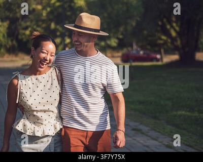 Ein glückliches junges Paar spaziert an einem warmen Sonnentag gemeinsam durch einen friedlichen Park. Stockfoto