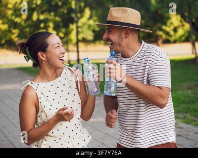 Junges Paar trinkt Wasser im Park an einem sonnigen Sommertag. Stockfoto