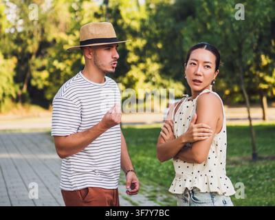 Frustrierter Mann, der während einer Meinungsverschiedenheit mit seinem Partner in einem sonnigen Park leidenschaftlich gestikuliert. Stockfoto