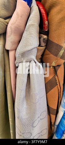 Nahaufnahme von gefalteten und verknoteten Schals in gedämpften Rosa-, Grau-, Oliv-, Braun- und Blautönen, die kontrastierende gewebte Muster und Texturdetails zeigen Stockfoto