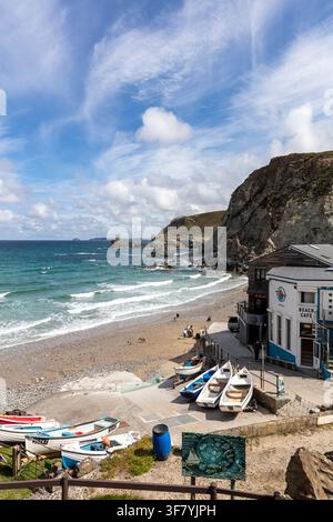 St Agnes an der Küste von Cornwall zeigt einen sandigen und kiesigen Strand mit kleinen Booten, die in der Nähe eines Strandcafés heraufgezogen sind. Felsenformationen umrahmen die Küstenlinie Stockfoto