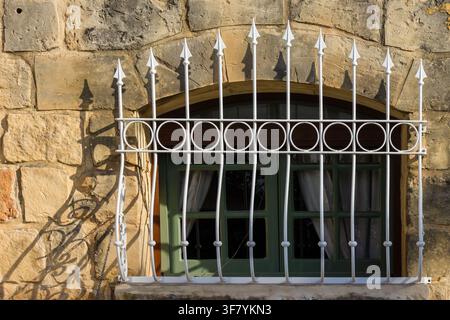 Grünes gewölbtes Fenster mit dekorativen weißen schmiedeeisernen Gittern an einer rustikalen Steinwand im Sonnenlicht Stockfoto