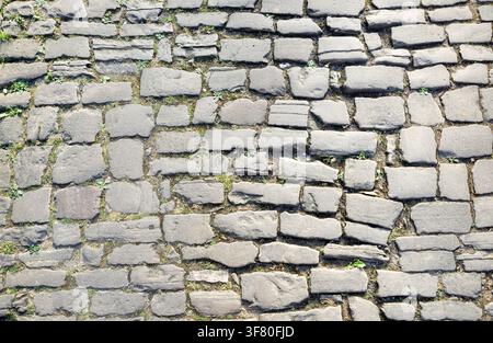Kopfsteinpflasterstraße aus abgenutzten Steinen mit Zwischenräumen, in denen Erde und Pflanzen wachsen. Blick von oben. Stockfoto
