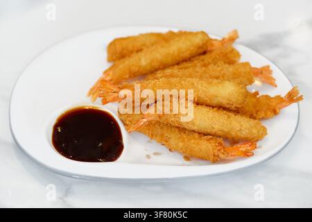 Hohe Blickwinkelaufnahme von goldenen, tiefgebratenen Ebi-Tempura-Garnelen, die auf einer weißen ovalen Platte serviert werden. Japanische panierte Garnelen-Vorspeise mit dunkler Dipsauce in einem Stockfoto