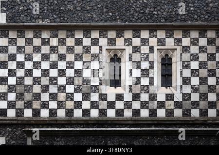 Schachbrettsteinmuster an einer mittelalterlichen Kirchenwand mit kleinen Fenstern zur Verwendung als Hintergrundtextur Stockfoto