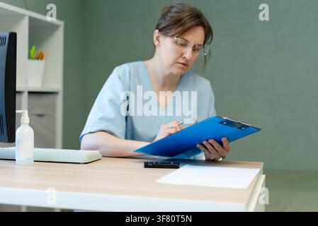 Professionelle Ärztin, die Akten an einem Schreibtisch in einer Arztpraxis durchsieht. Konzentrierte Ärztin studiert Dokumente in einem ruhigen Beratungsraum. Engagierte Gesundheitsfachkraft untersucht Gesundheitsdaten Stockfoto
