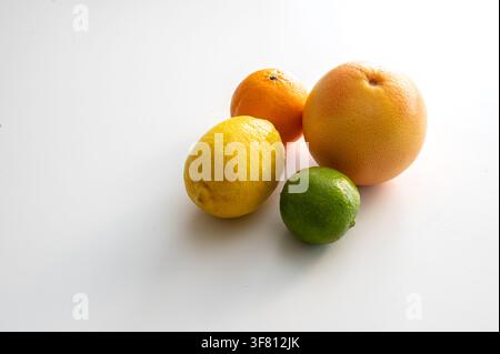Eine reife Zitrone, Limette und rosa Grapefruit, angeordnet auf einer hellen weißen Oberfläche, eine einfache minimale Stillleben-Komposition aus frischen Zitrusfrüchten, reich an Vitamin C, für eine gesunde Sommererfrischung. Stockfoto