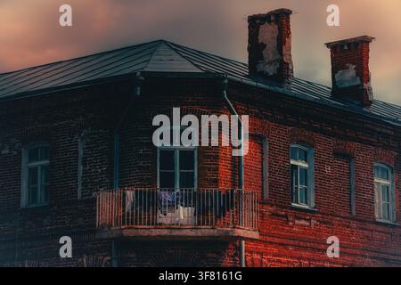 Architektonisches Fragment eines alten traditionellen Backsteinhauses mit Fenstern und weißer Wäsche, die an einem Balkon hängt. Stockfoto