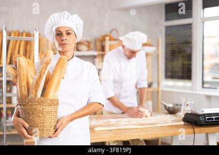 Porträt einer positiven Bäckerin, die einen Korb mit Baguettes und frischem Brot in der Hand hält Stockfoto