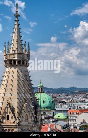 Hohe Blickwinkelansicht des steinernen Turms der St. Stephans-Kathedrale und der grünen Kuppel der St. Peters-Kirche unter blauem Himmel in Wien Stockfoto