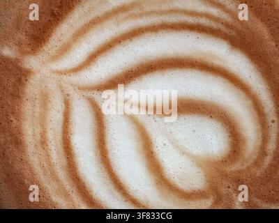 Abstrakte Nahaufnahme von Latte Art und Milchschaumtextur. Extrem Nahaufnahme von cremiger Latte Art, zartem weißem Milchschaum, geschwungenen Kaffeemustern. Abstrakt Stockfoto