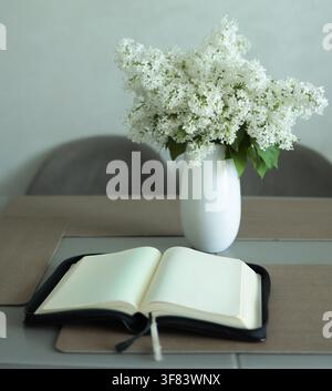 Offenes leeres Buch und weißer Fliederstrauß in einer Vase auf Holztablett mit drei leeren Bilderrahmen an der Wand, Innenraum-Modell. Stockfoto