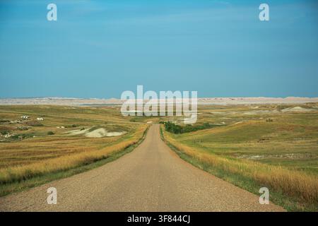 Schotterstraße, die sich bis zum Horizont durch offene Ebenen im Badlands Nationalpark, South Dakota, USA erstreckt Stockfoto