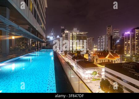 Blick auf den Pool bei Nacht mit Blick auf Stadtgebäude und die St.-Joseph-Kirche in Singapur Stockfoto