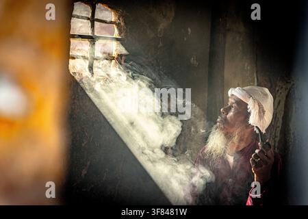 Ein Mann raucht eine Pfeife am Fenster, während Licht einfällt, und zeigt das tägliche Leben in Vietnam Stockfoto