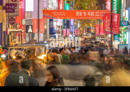 Einkäufer schlendern zwischen Neonlichtern auf der Myeongdong-Einkaufsstraße in Seoul bei Nacht mit farbenfrohen Ständen und geschäftiger Atmosphäre Stockfoto